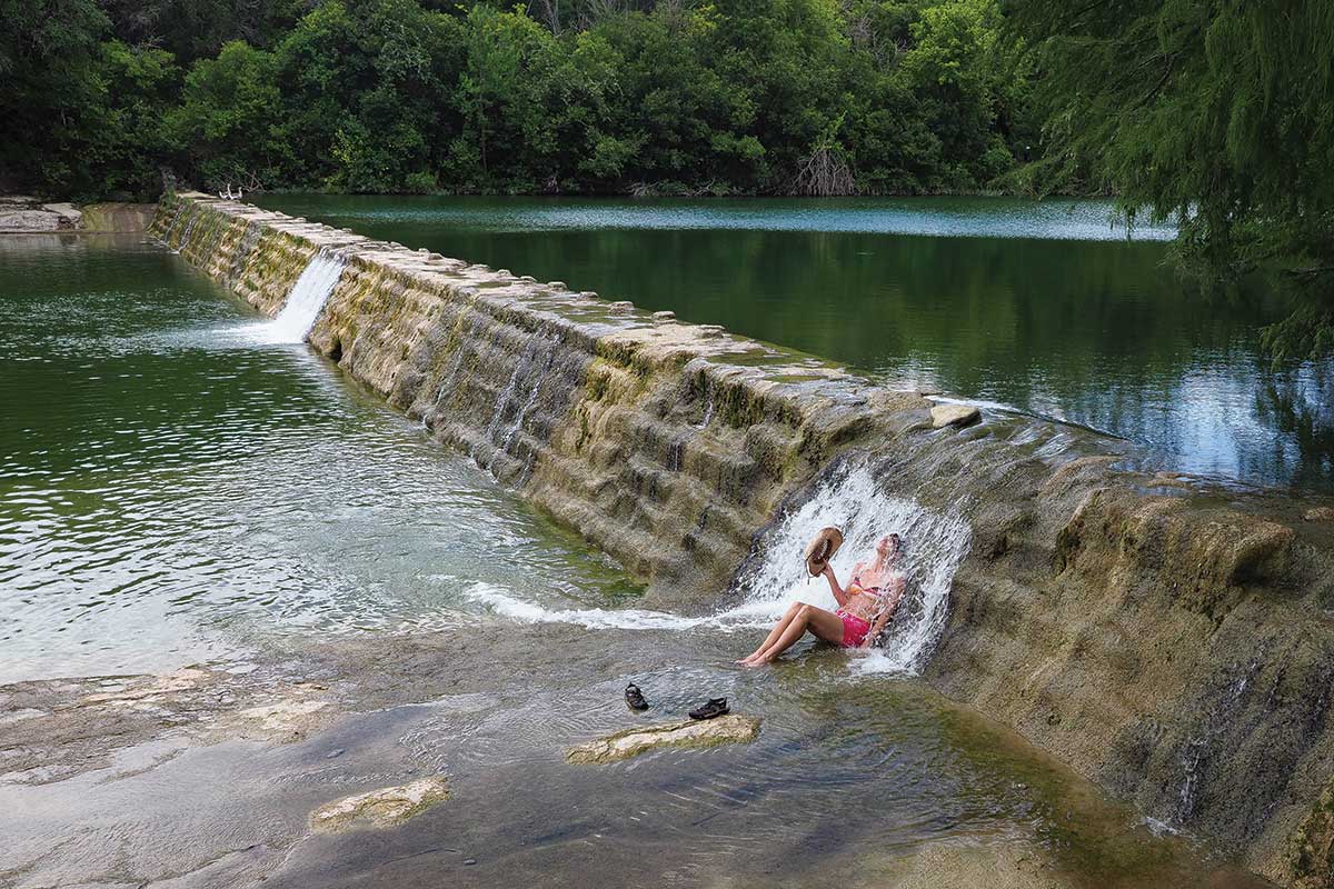 author sits under small waterfall at Blanco State Park
