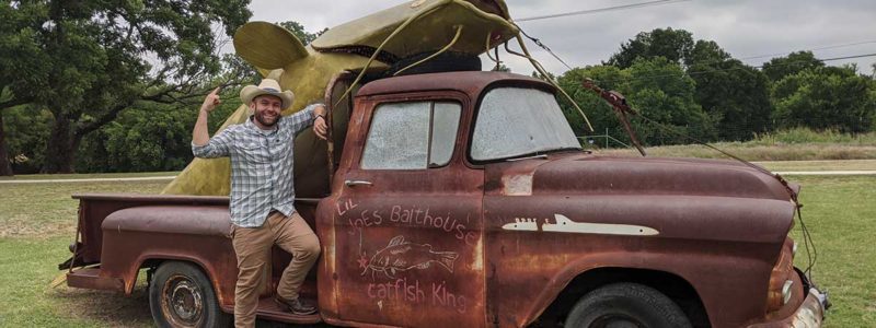 Chet stands in front of an old truck with a giant catfish in the bed