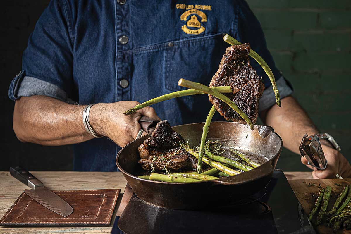 man cooking and flipping asparagus in a cast-iron pan
