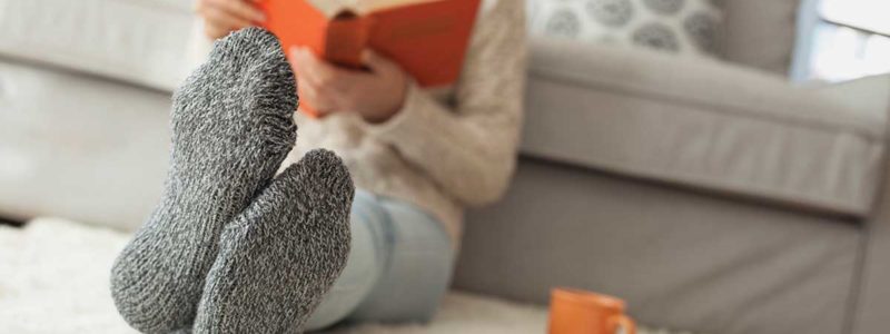 Woman in cozy socks and coffee mug reading a book on a furry rug