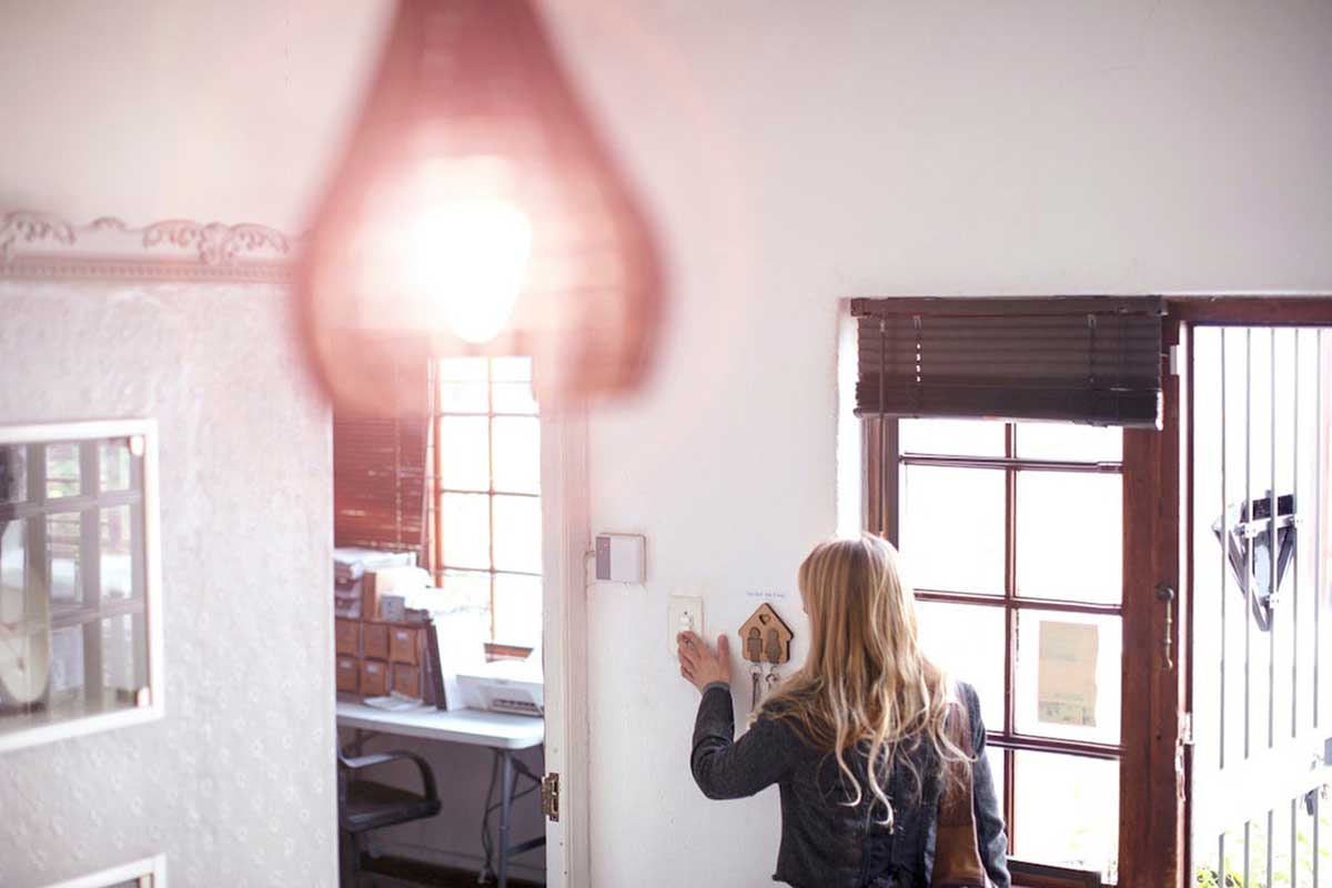 A light bulb in the foreground of a photo with a woman inside a home