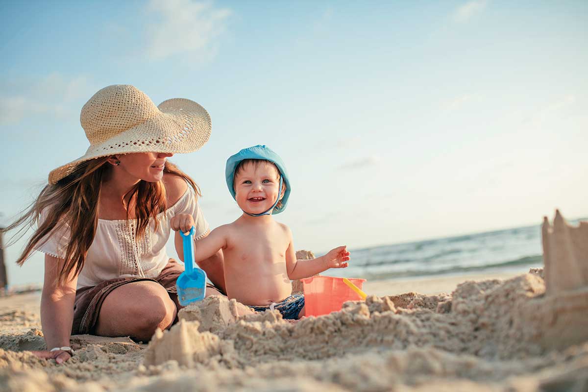 mom building sand castle on beach with young son