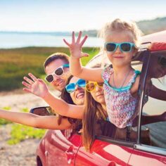 a cute family in sunglasses hanging out car windows at the beach