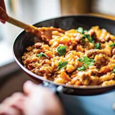 Hands with spatula stirring and cooking food in a skillet